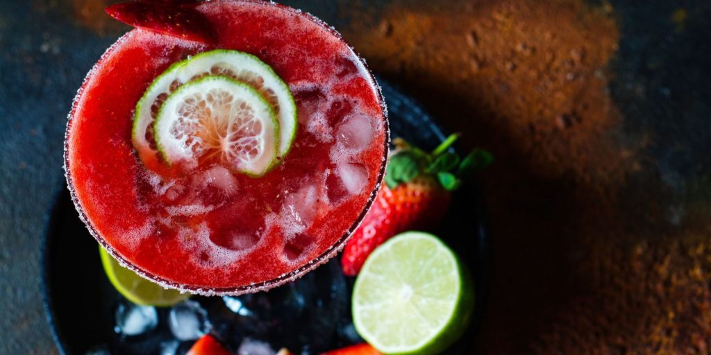 Overhead shot of a strawberry margarita with slices of lime on a wooden surface