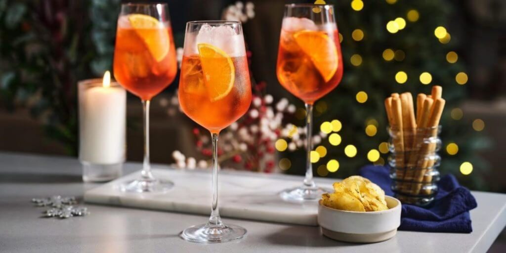 Three Aperol Spritz cocktails with festive decor in the background