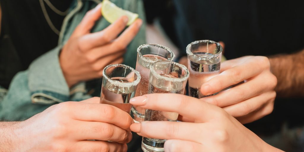 Cropped view of interracial friends holding glasses of tequila with salted rims at a bar; image by LIGHTFIELD STUDIOS via Adobe Stock.