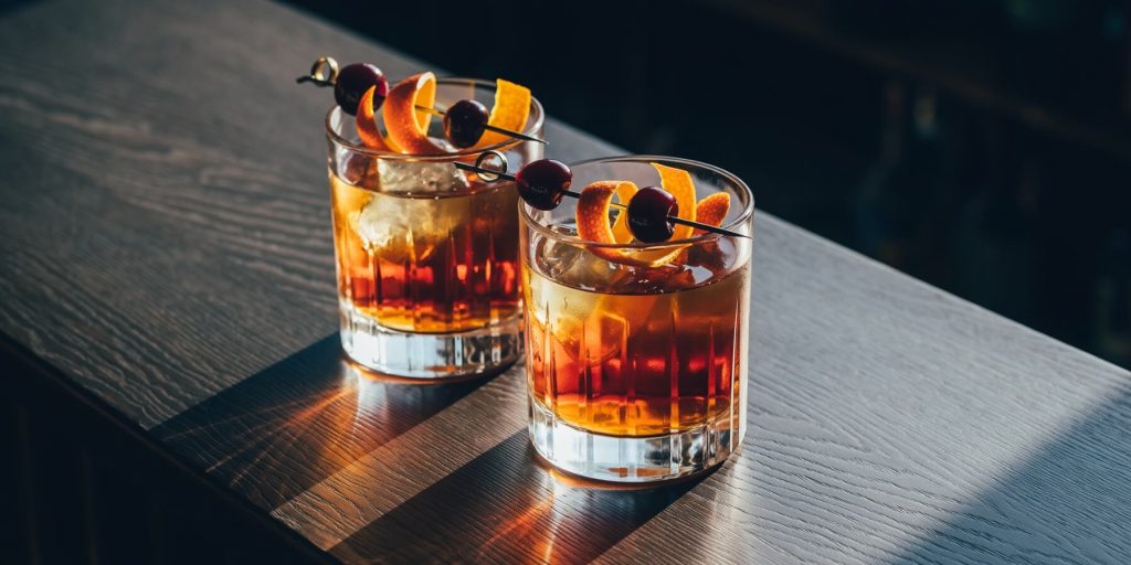 Two Maple Old Fashioned cocktails with dark cherry and orange peel garnish