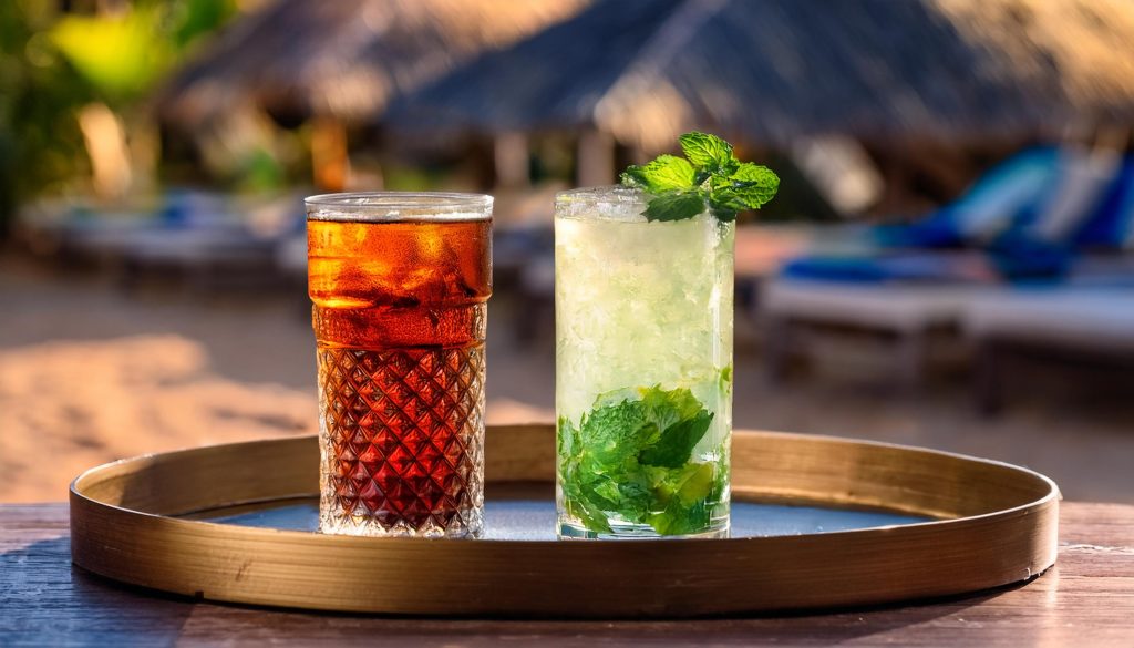 A Cuba Libre and a Mojito on a tray in a beach setting