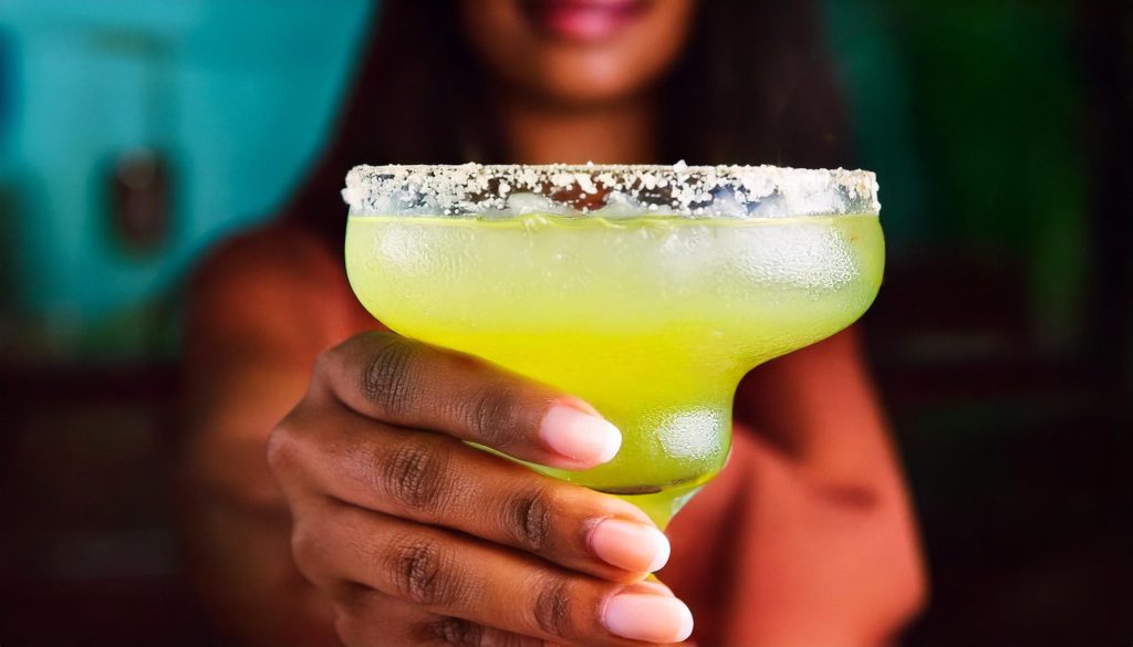 Close-up of a woman's hand holding a Margarita with salted rim to camera