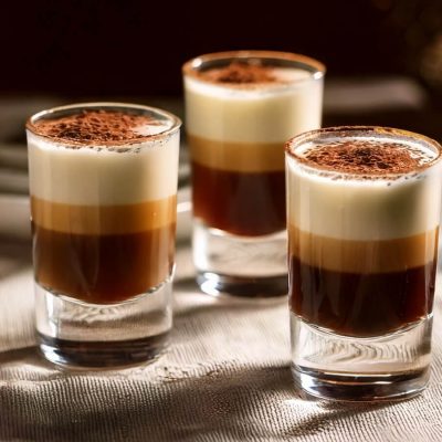 Three layered Tiramisu Shots in shot glasses, featuring dark coffee, creamy liqueur, and a dusting of cocoa powder on top.