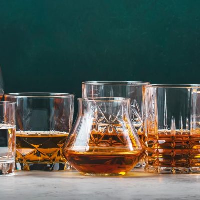 Wide variety of brandy glasses with golden and amber liquids, arranged on a marble table, photo by 5ph/Adobe Stock