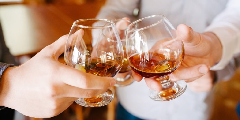 Three people clinking snifters of aged brandy in a celebratory toast, photo by ruslan_shramko/Adobe Stock