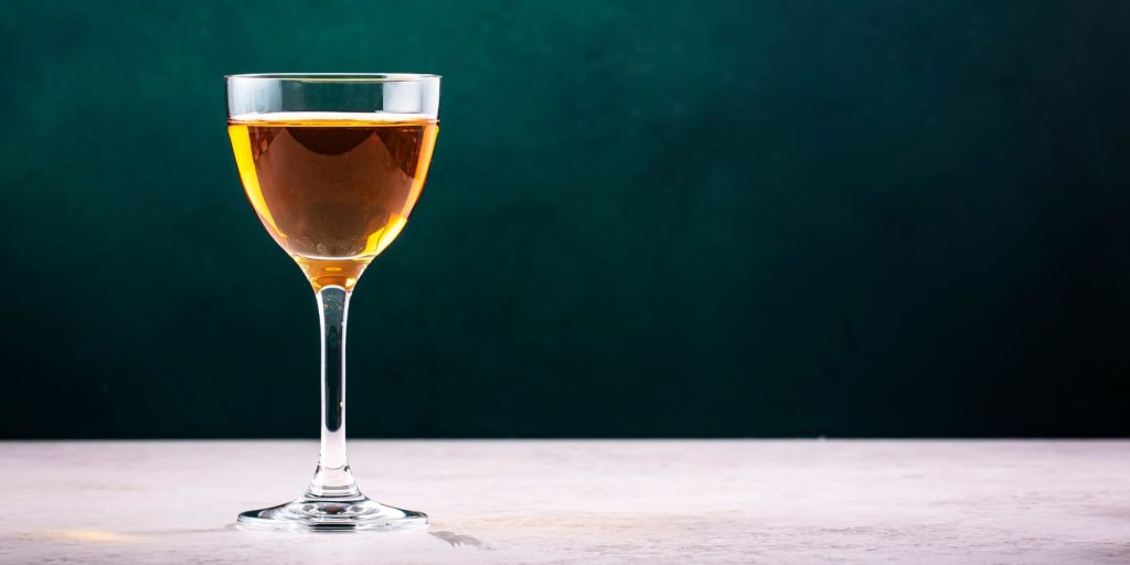 Stemmed glass of pomace brandy against a green background, photo by 5ph/Adobe Stock