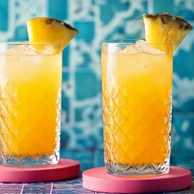 Two vibrant Desert Diablo Pineapple and Tequila cocktails against a pale blue tiled background