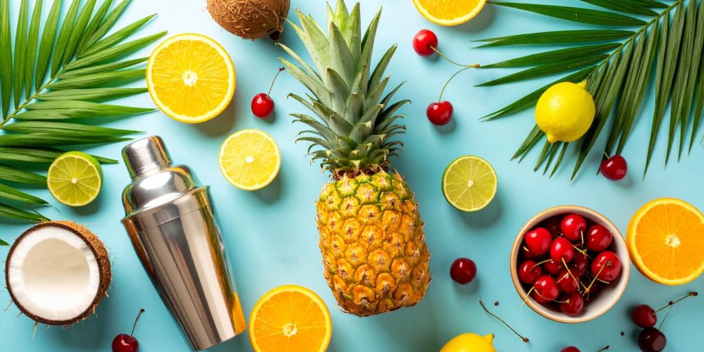 Flat lay of ingredients used to make the best tropical drinks including pineapple, coconut, limes, oranges and cherries
