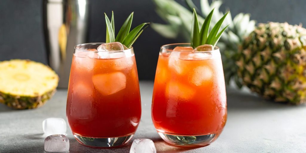 Two amber red Jungle Bird cocktails with pineapple frond garnish