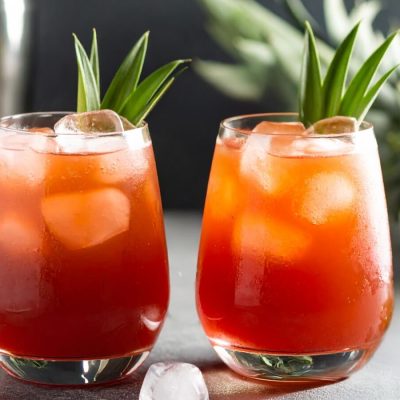 Two amber red Jungle Bird cocktails with pineapple frond garnish