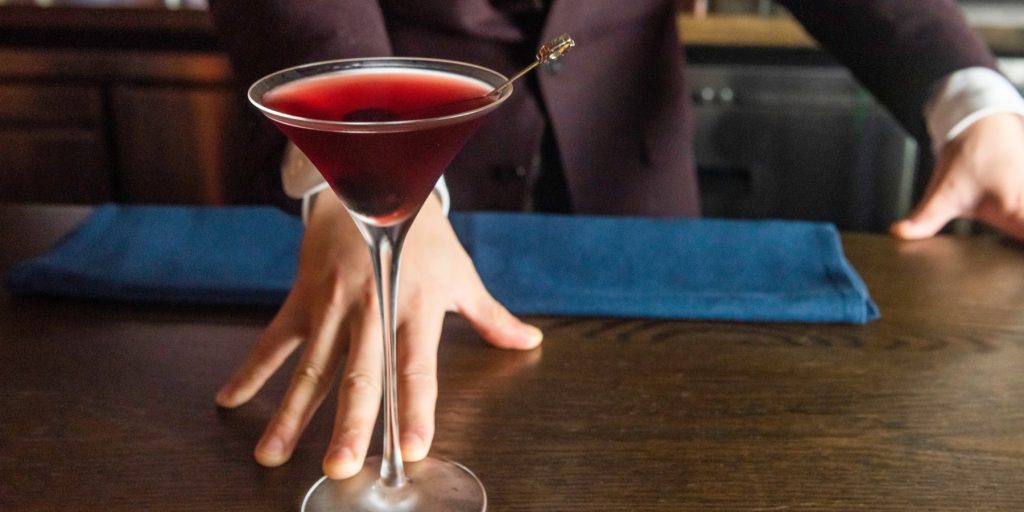 Close up of Takuma sliding a Grand Martiny's cocktail over a bar counter
