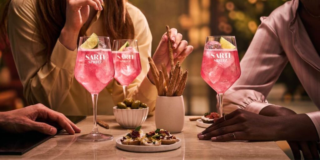Three friends around a table enjoying Sarti Spritz cocktails alongisde aperitivo bites in the golden light of the late afternoon.