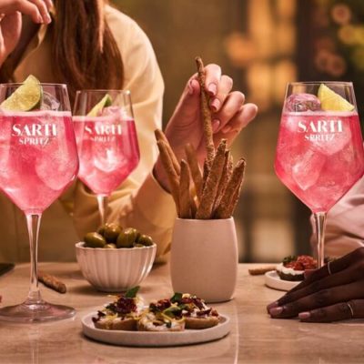 Three friends around a table enjoying Sarti Spritz cocktails alongisde aperitivo bites in the golden light of the late afternoon.