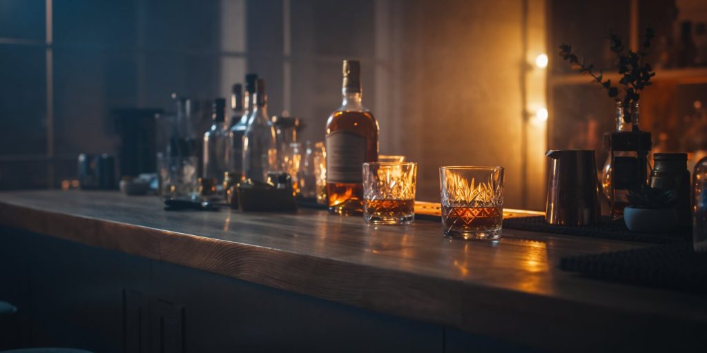 A cosy bar set up at home with moody lighting two glasses of whiskey with bottles in the background
