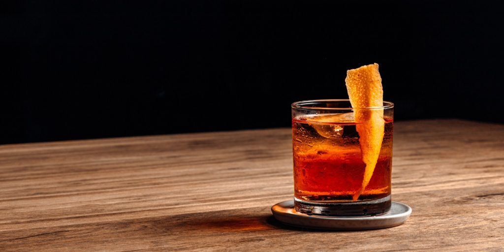 A negroni cocktail on a wooden surface with an orange peel garnish