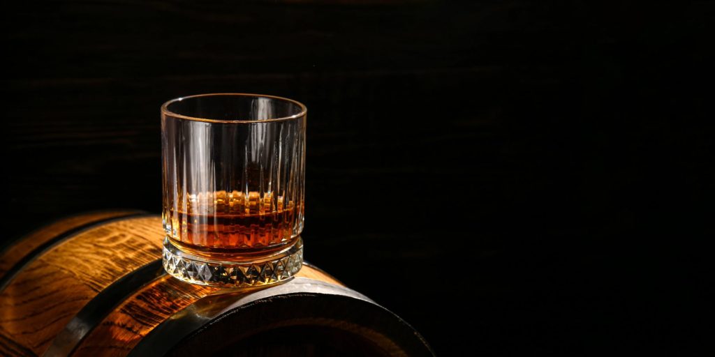 A straight bourbon in a rocks glass on top of a barrel