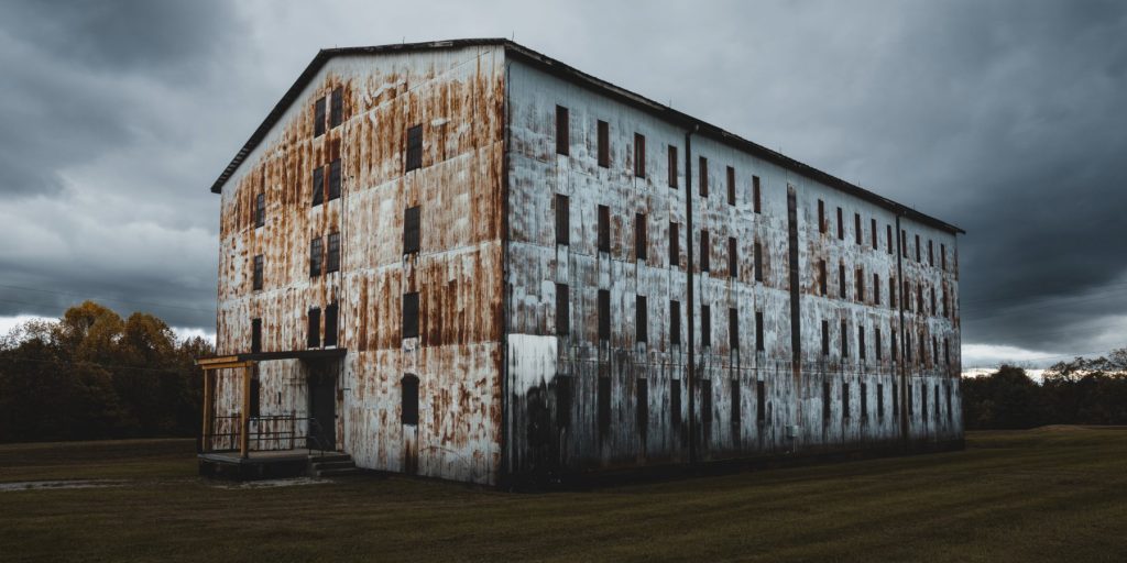 A weathered bourbon rickhouse in a field.