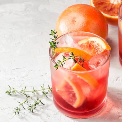 Two blood orange Aperol spritz cocktails garnished with fresh slices of orange and thyme.