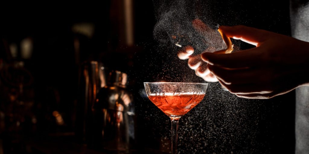 A side shot of a bartender expressing orange peel oils over a Aperol cocktail.