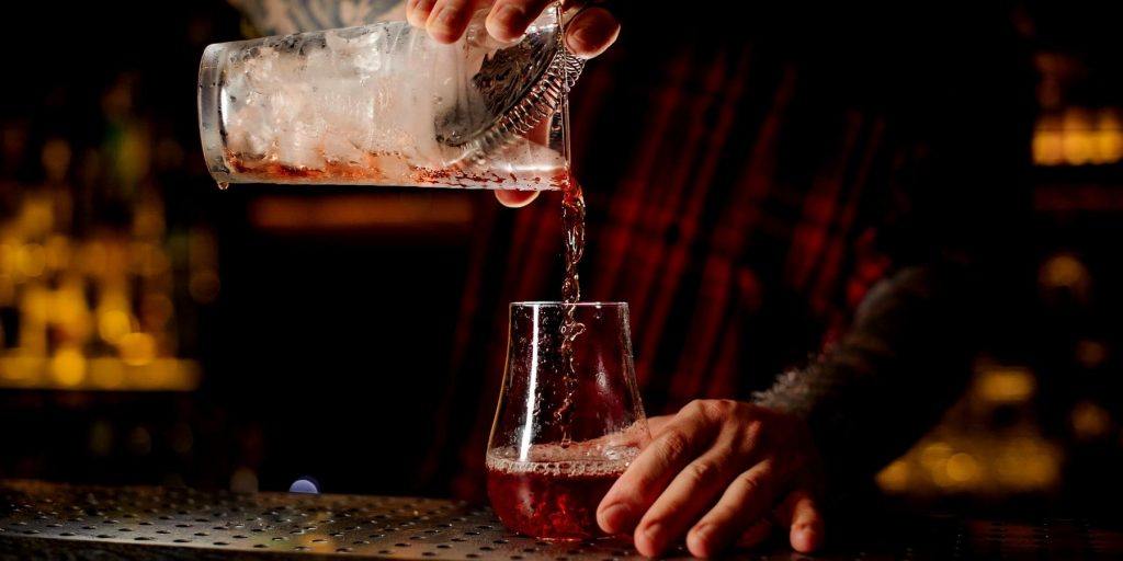 Close up of a bartender pouring an Aperol Eclipse cocktail in a moody bar backlit in sihouette