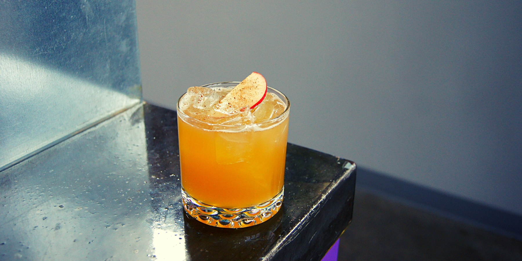 A Rustic Apple Manhattan cocktail with a rich, amber hue, garnished with apple slices and cinnamon.