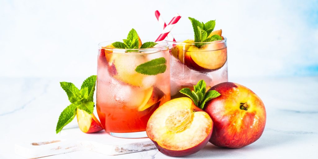 Two Ginger Peach Sparkle cockgtails on a white marble counter against a white backdrop in a light bright home kitchen