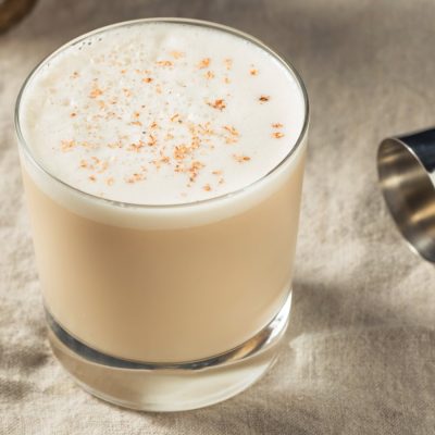 A Brandy Milk Punch cocktail in a rocks glass on a table with a cocktail jigger