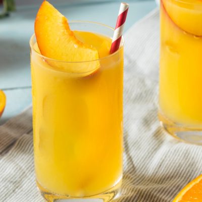 Fuzzy Navel cocktail in a highball glass with sliced peach garnish