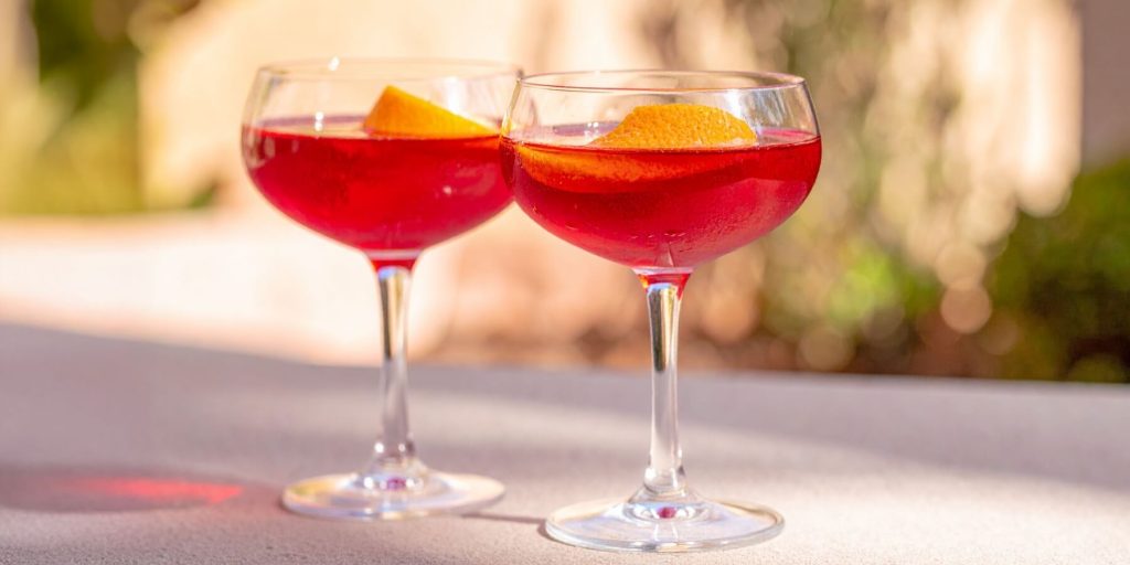 Two Negroni Up cocktails in coupe glasses with orange peel garnish, served in a courtyard