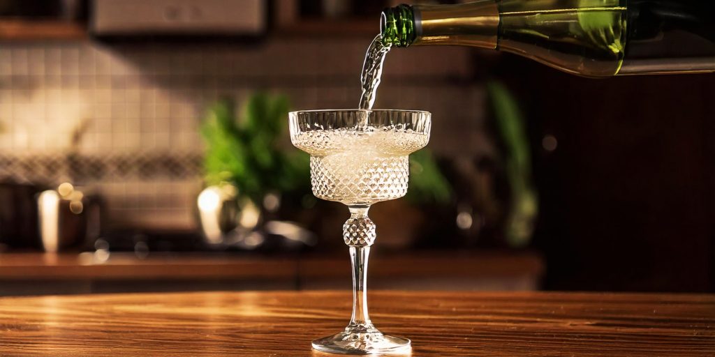 Pouring shot of Champagne into a retro coupe glass