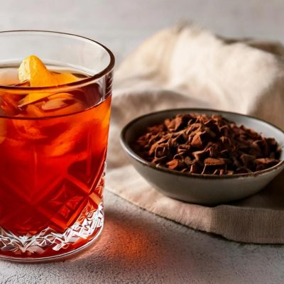A burnt amber colored London Fog cocktail next to a bowl of cocoa nibs