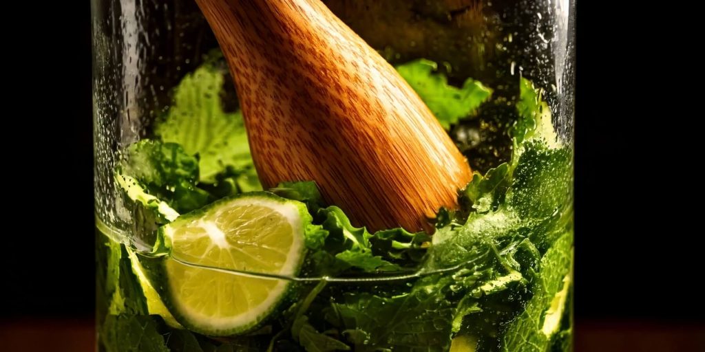 Close-up of a wooden muddler inside a glass jar of muddled shiso leaves and lime