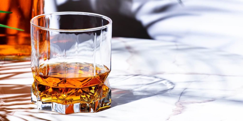 Close-up of a faceted glass of American brandy on a white marble table, photo by 5ph/Adobe Stock