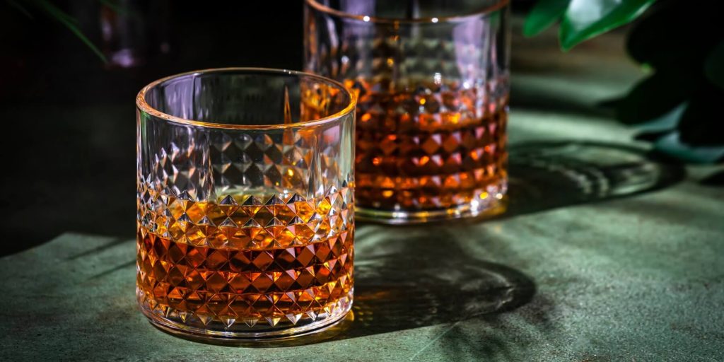 Two glasses of amber South African brandy on a green table with moody lighting, photo by 5ph/Adobe Stock