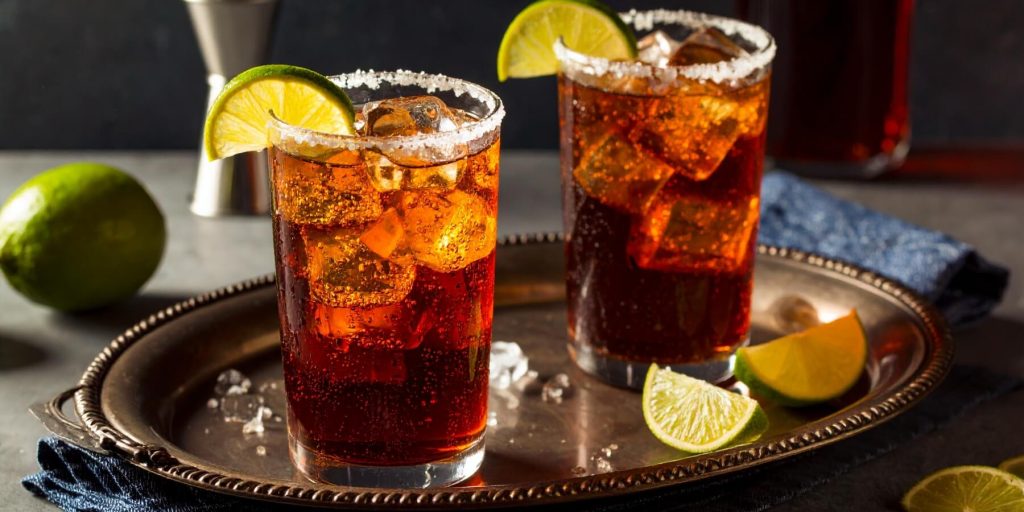Two Batanga cocktails served in salt-rimmed highball glasses with lime wedge garnish