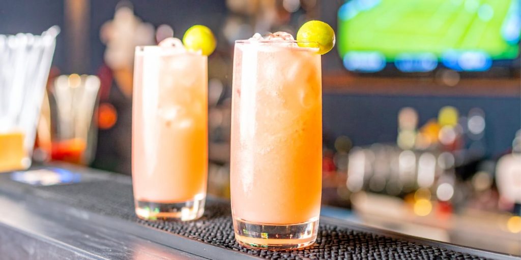 Two Honey Deuce cocktails with honeydew melon garnish, bar in the background