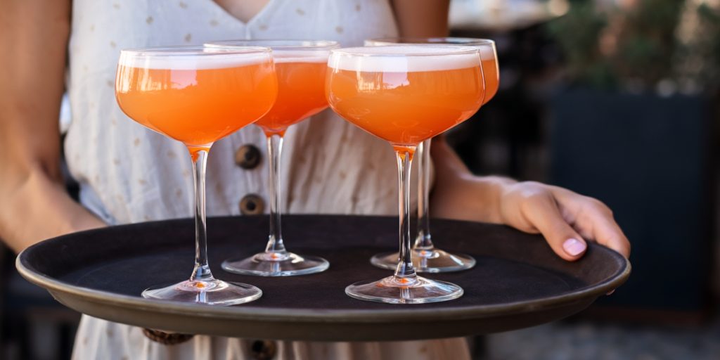 Woman in summer dress holding black tray of 4 Aperol cocktails
