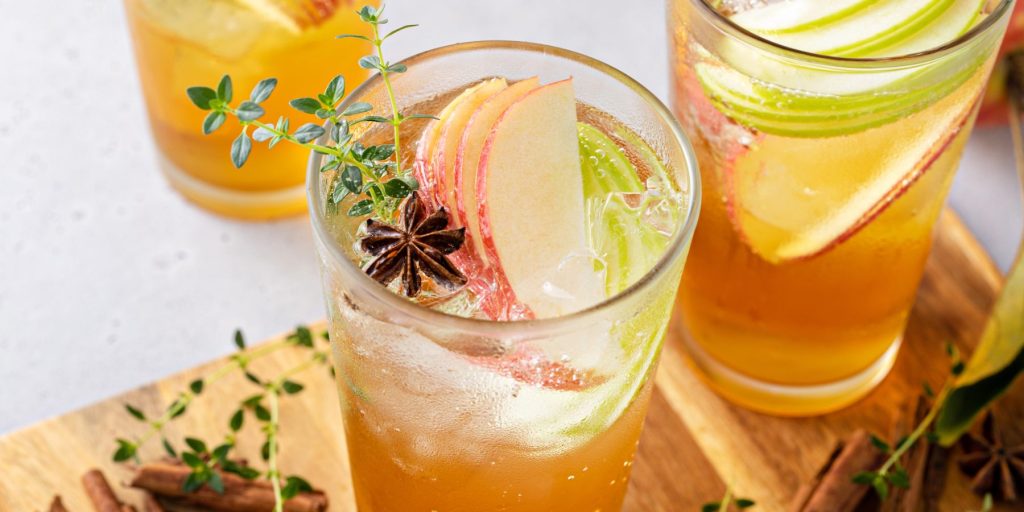 Two apple cider spritz cocktails garnished with fresh apples slices, thyme and star anise.