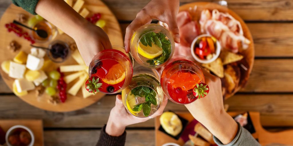 A top shot of a table with snacks and a friends toasting with cocktails.
